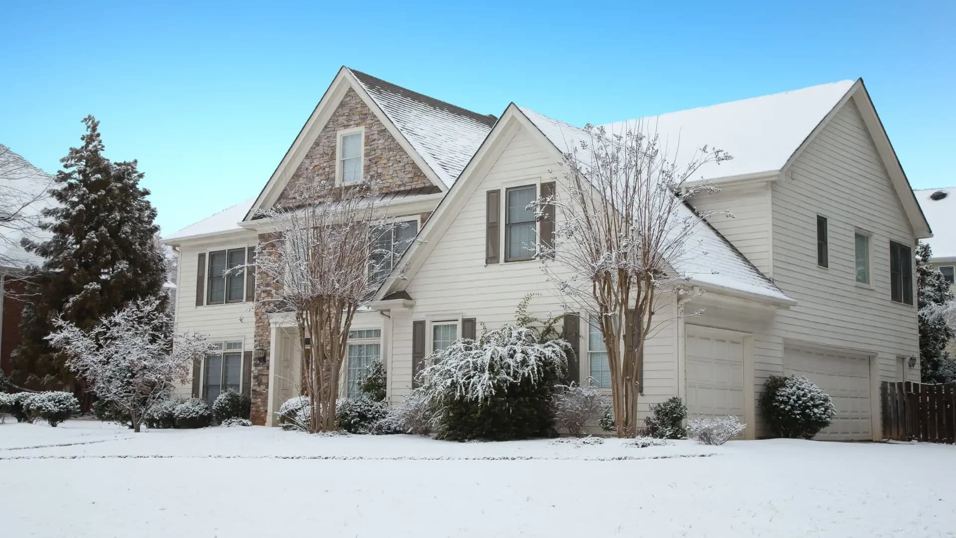 A snow-covered house with white siding and partial stone facade.