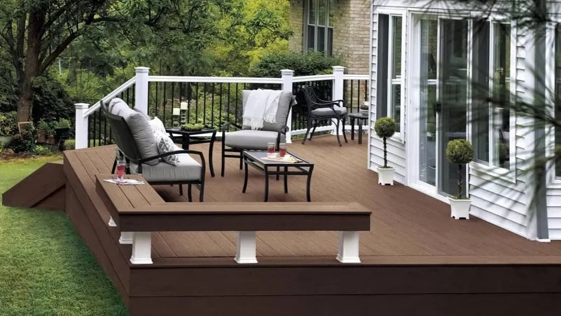 A new brown-colored deck with patio furniture, built-in bench, and white and black railing.