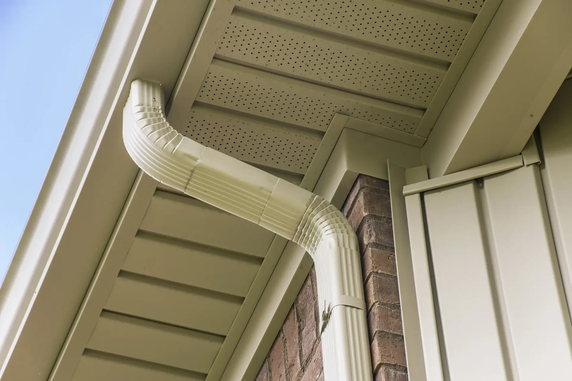 Tan gutters, downspout, and soffit on a brick house.