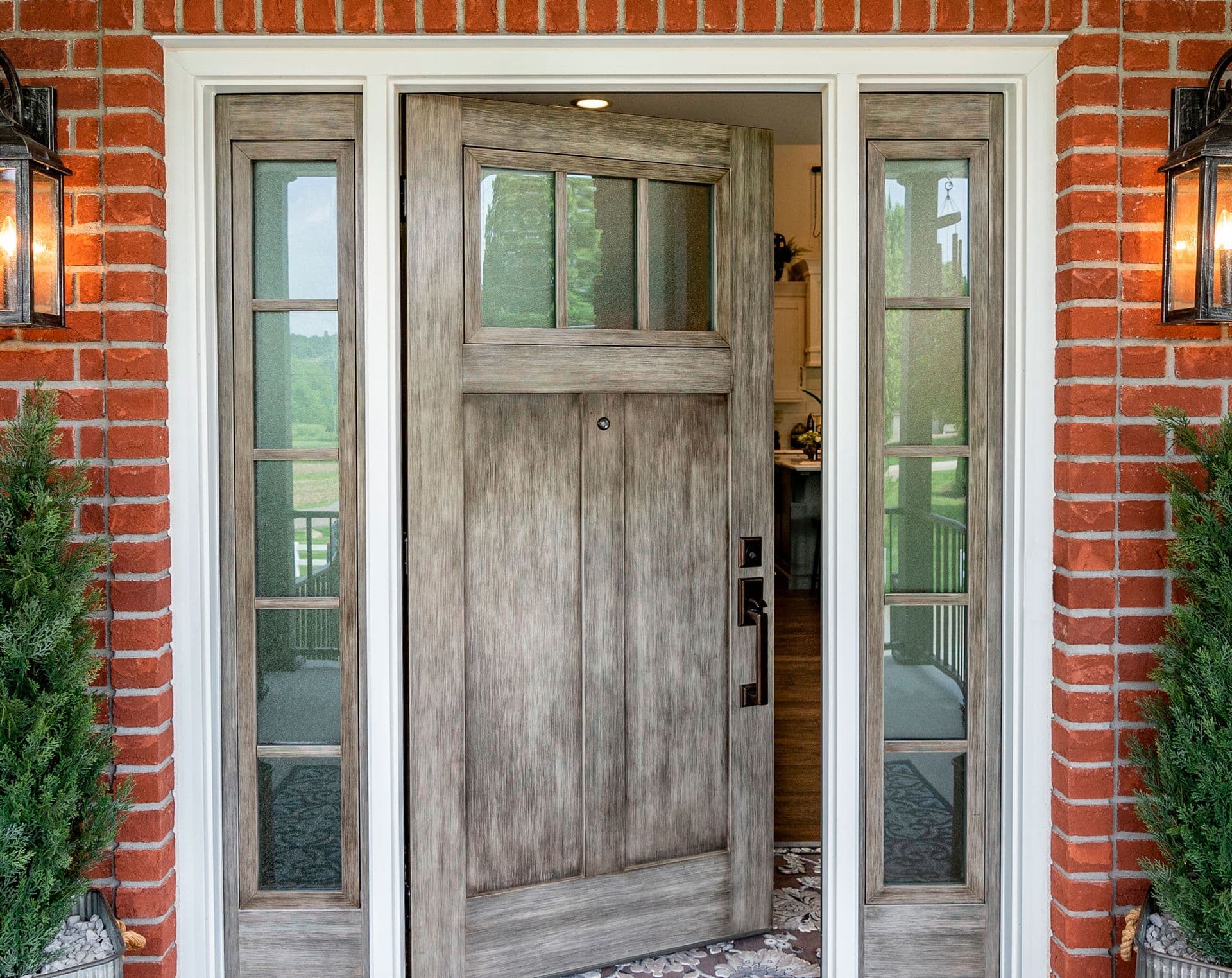 A ProVia Signet fiberglass fir door and sidelites in Natural Leather gray glaze on the porch of a red brick home