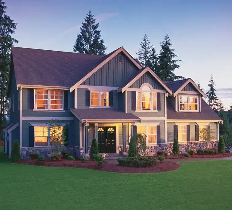 A green house with light-colored trim, black double front door and black shutters at dusk.