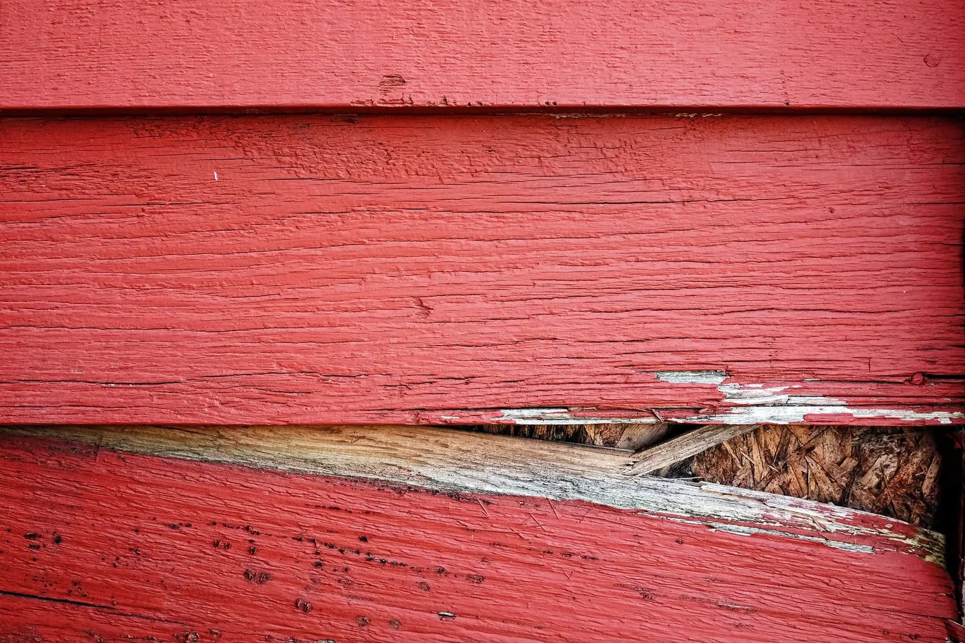 A close-up of damaged red siding on a house.