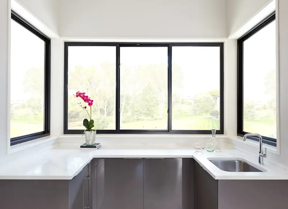 Slider windows with matte black trim in a modern kitchen with white countertops.